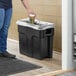 A person putting a cup into a black Toter Slimline trash can.