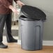 A person putting garbage in a dark gray Toter trash can with a black lid.