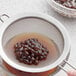 A person using a sieve to strain brown Fanale U.S. Tapioca Boba Pearls.