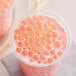 A plastic cup of pink bubble tea with Fanale lychee popping boba and bubbles in it.