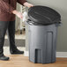 A man standing next to a Toter dark gray trash can with a black lid.