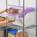 A woman using a scoop to pour cereal into a Baker's Mark purple ingredient bin.