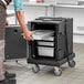 A man in a chef's uniform using a black front loading insulated container to hold metal trays.