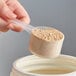 A hand holding a 43 cc Polypropylene scoop with protein powder in it.