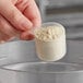 A hand holding a 25 cc polypropylene scoop full of powder.