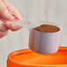 a hand holding a measuring cup with brown powder