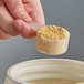 A hand using a Polypropylene scoop to measure yellow powder into a container.