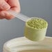 A hand using a long-handled Polypropylene scoop to measure green powder.