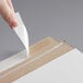 A hand using tape to seal a piece of paper in a white rigid mailer.