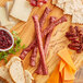 A cutting board with Shaffer Venison Farms Venison Snack Sticks, cheese, grapes, and crackers on a table.