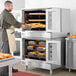 A man wearing an apron putting food into a Cooking Performance Group double deck convection oven.