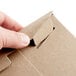 A hand opening a Lavex Stayflats kraft mailer box.