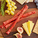 A wooden cutting board with cheese, grapes, and Shaffer Venison Farms Wild Boar Snack Sticks.