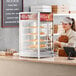 A woman standing behind a countertop display case with pizza.