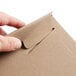 A hand opening a Lavex Stayflats kraft brown envelope with a piece of cardboard inside using a paper clip.