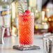 An Acopa Aurelius beverage glass with a red cocktail and a sprig of rosemary on a stone coaster.