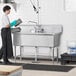 A woman in a black apron using a Regency stainless steel three compartment sink in a professional kitchen.