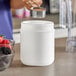 A person pouring brown powder into a 55 oz. white plastic canister.
