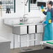 A man in a blue uniform and gloves using a Regency 3 compartment sink in a professional kitchen.