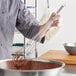 A person using a Choice stainless steel French whisk to mix chocolate in a bowl.