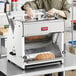 A woman in a kitchen using an Estella countertop bread slicer to slice bread.