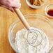 A hand mixing dough in a bowl with a Choice stainless steel Danish dough whisk with a wood handle.