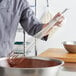 A person using a Choice stainless steel French whisk to mix chocolate batter in a bowl.