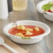 A Dixie Ultra Pathways paper bowl of soup with a white spoon on a table.