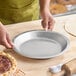 A round, shallow aluminum pie pan being held over a wooden surface.
