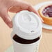 A hand holding a white plastic lid on a coffee cup.