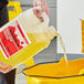 A person pouring Sierra by Noble Chemical concentrated floor finish emulsifier from a yellow jug into a bucket.