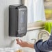 A woman using a Pacific Blue Ultra touchless hand sanitizer dispenser on a counter.