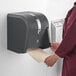 A person in a red shirt using a black Georgia Pacific Pro Universal Push Paddle paper towel dispenser.