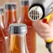 A person using a hot air gun to shrink a clear plastic band around a bottle with a plastic cap.