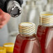 A blurry close-up of a person's hand pouring honey over a jar of jam with a red perforated shrink band.