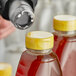 A person's blurry hand pouring a clear shrink band onto a bottle of yellow liquid.