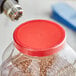 A person uses a drill to add a 1" clear non-perforated shrink band to a plastic container with a red lid.