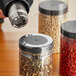 A person using a 2" clear perforated shrink band on a jar of peppercorns with a plastic lid.