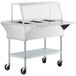 A silver ServIt electric steam table with clear sneeze guard on wheels.