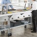 A man and woman in a kitchen using a ServIt electric steam table with sneeze guard and tubular tray slide.