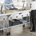 A man and woman standing in a school kitchen with a ServIt electric steam table with a sneeze guard.