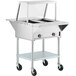 A ServIt stainless steel electric steam table on wheels with an angled glass sneeze guard.