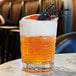 A close up of an Arcoroc Brixton rocks glass filled with an orange drink and a flower.