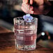 A person holding a flower in an Arcoroc Brixton rocks glass filled with liquid and ice.