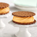 Two Creamery Ave. Cantaloupe Soft Serve Mix ice cream sandwiches on white pedestals.