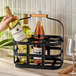 A hand holding a bottle of wine in a Franmara black metal wine bottle caddy on a table.