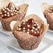 A chocolate cupcake with Mona Lisa white chocolate frosting and white Crispearls on a plate.