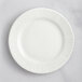 A close up of a white RAK Porcelain flat plate with wavy lines on the rim.