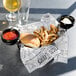 A black fluted ramekin filled with white sauce on a counter with a basket of food and a hamburger.