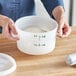 A woman holding a white Vigor food storage container with white dough inside.